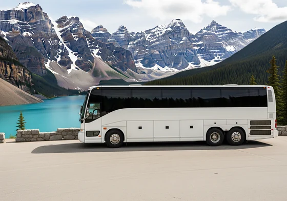 A large white touring coach parked at a mountain viewpoint, with snow capped peaks and a lake behind it.