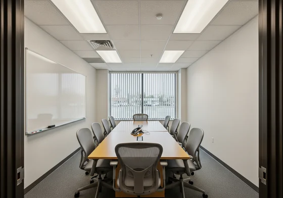 A small workplace meeting room with a long table, ten chairs and a large whiteboard on one wall.